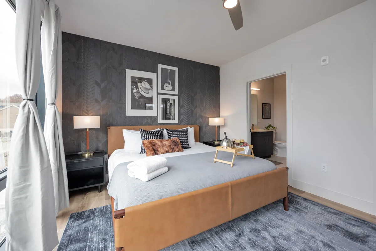 A cozy second bedroom featuring a bed with a brown leather headboard, elegant wall artwork, nightstands with lamps, and soft, inviting textures. The space feels both stylish and comfortable, ideal for restful nights.