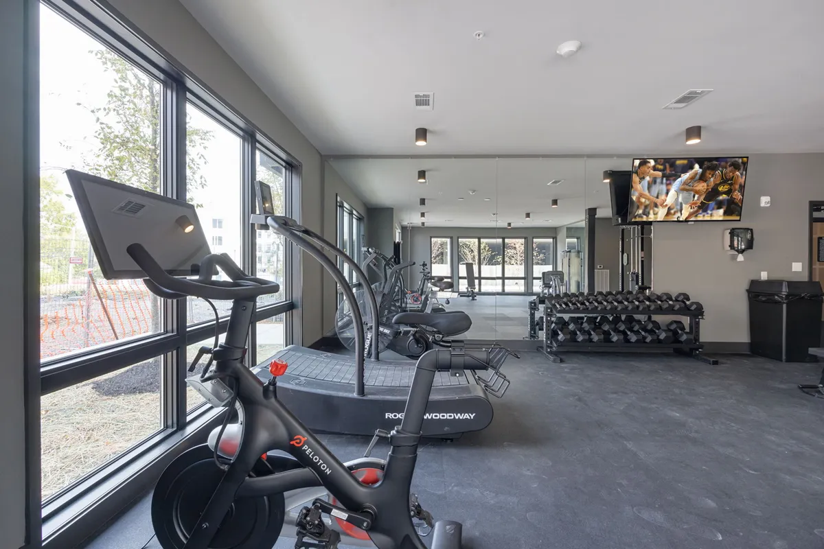 A modern fitness center with a Peloton bike, treadmill, free weights, large windows bringing in natural light, and a TV screen. The space feels bright, motivating, and well-equipped for business travelers to maintain their fitness routines.