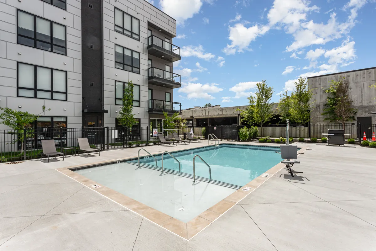 A beautifully maintained outdoor swimming pool surrounded by a modern building facade and lined with comfortable lounge chairs. Lush greenery adds a resort-like feel, and the inviting pool area is ready for sunbathing, swimming, or socializing.