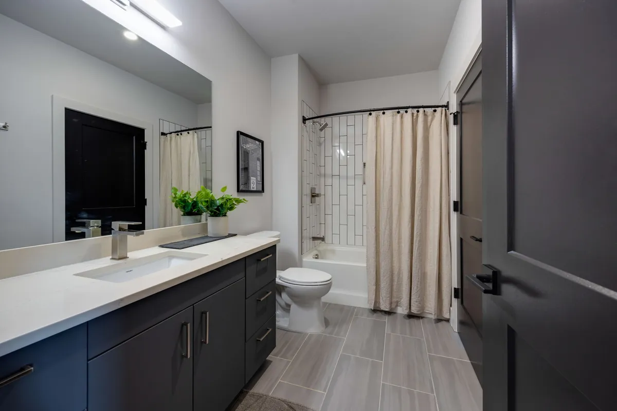A refreshing en-suite bathroom with a vanity and sink, a bathtub for relaxing, framed wall art, and a touch of greenery. The serene setting is perfect for unwinding or preparing for the day.