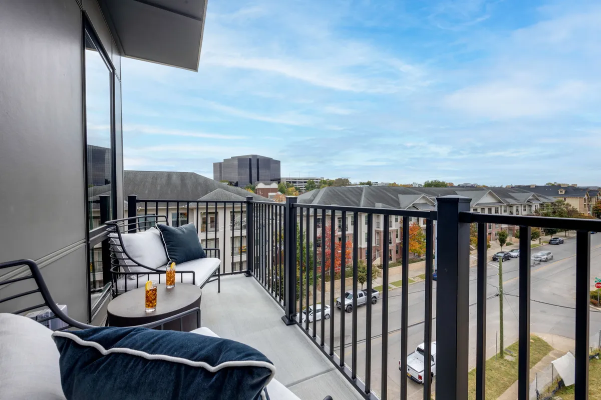 This image features a cozy balcony or patio area with seating, a decorative table, a glass with a beverage, and a stunning city view. It creates a serene, inviting atmosphere perfect for morning coffee or evening relaxation.